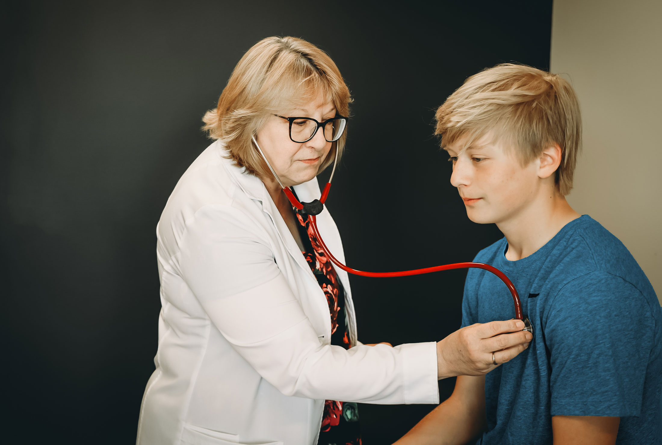 Doctor listening to teen boy's heart using a stethoscope